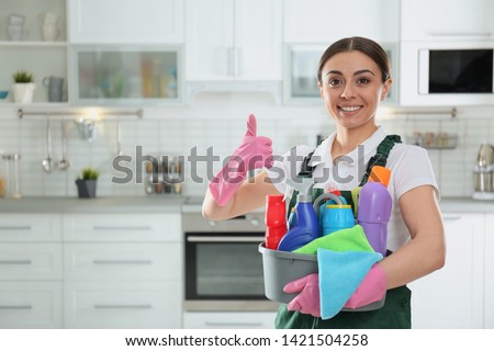 Portrait of young woman with basin of detergents in kitchen. Cleaning service Royalty-Free Stock Photo #1421504258