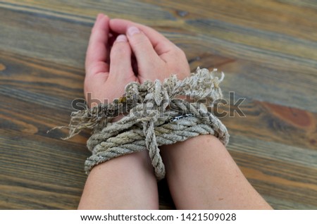 Woman's hands tied with an old rope, the rope is gray with age and unraveling at the ends. It is possible to interpret the picture as torture or as a tie for the time being.