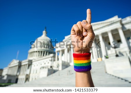 Hand wearing gay pride rainbow wristband holding up number one index finger outside the Capitol Building in Washington, DC, USA