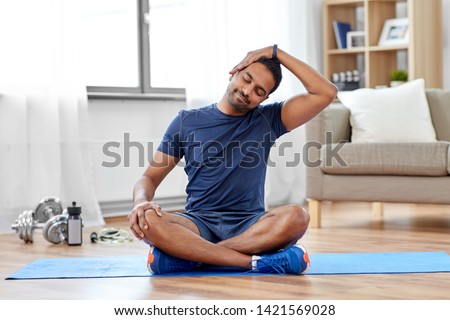 sport, fitness and healthy lifestyle concept - indian man training and stretching body at home Royalty-Free Stock Photo #1421569028