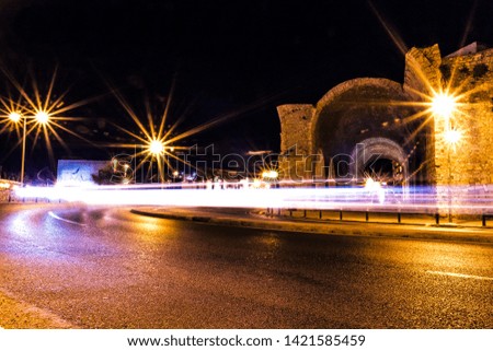 long exposure photo of car light trails on a turning road next to old heraklion city ruins