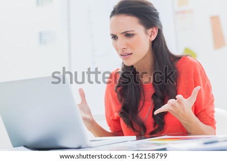 Annoyed designer gesturing in front of her laptop in her office Royalty-Free Stock Photo #142158799