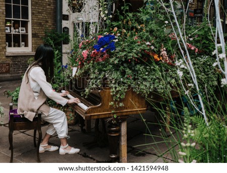Woman playing piano decorated with flowers at Covent Garden, London. Side view.