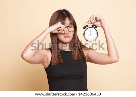 Sleepy young Asian woman with a clock in the morning  on beige background