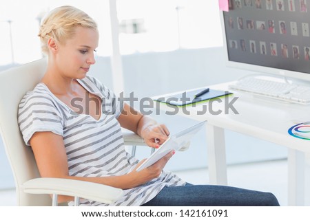 Blonde photo editor working on a tablet computer in her office