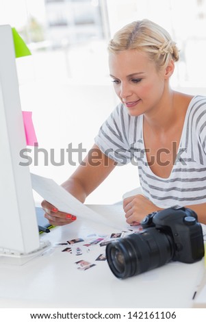 Cheerful photo editor looking at a contact sheet with a digital camera on her desk