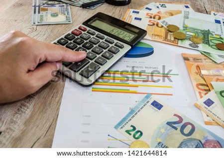 hand is typing something on a calculator against the background of business graphics, dollars and euros