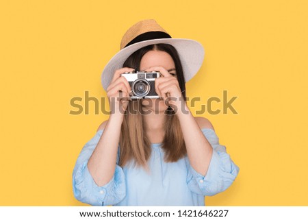 Young woman photographer tourist standing isolated over yellow background holding camera