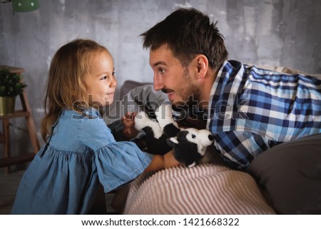 Dad and his daughter are playing in the bedroom. Plush doggy in the hands of. Daddy's baby. Dad with a beard in a plaid shirt, a girl in a denim dress. Happy family. Father's day