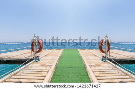 Wooden jetty with green carpet and lifebuoys on a peaceful summer sea beach.