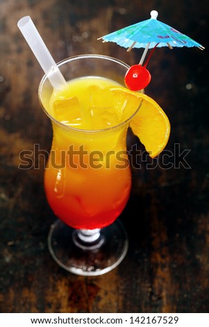 High angle view of a tall glass of orange daiquiri cocktail served with a straw and garnished with a red cherry on a cocktail umbrella for a festive party celebration