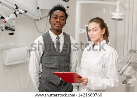African male patient in dental clinic. Young Woman dentist makes a diagnosis and records recommendations. Medicine, health, stomatology concept. dentist treating a patient.