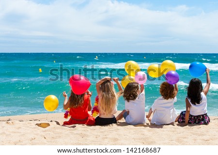 Young kids holding color balloons sitting on beach.