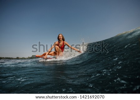 Woman in red swimsuit with loose long hair surfs in a sea