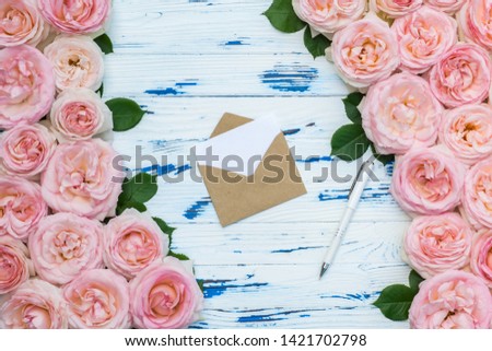 Flowers composition with open craft paper envelope and pen in the frame made of pink roses on aged wooden background.