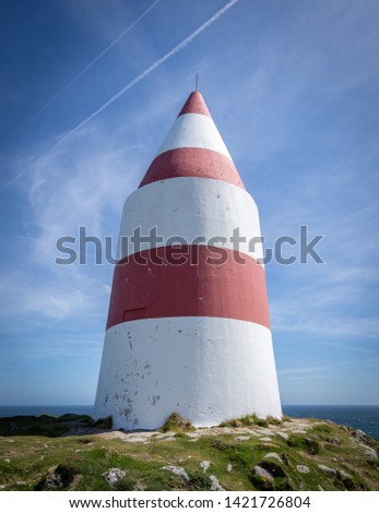 The red and white striped Daymark beacon on St Martins Island, the Isles of Scilly, Cornwall warns maritime vessels of hidden rocks. The beacon is set against a blue sky.