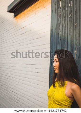 Asian woman in a festive yellow lace dress stands near the white brick wall, view from above