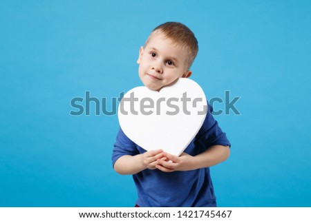 Smiling fun kid boy 4 years old wearing blue t-shirt clothes hold in hand white heart isolated on blue wall background children studio portrait. People childhood lifestyle concept. Mock up copy space