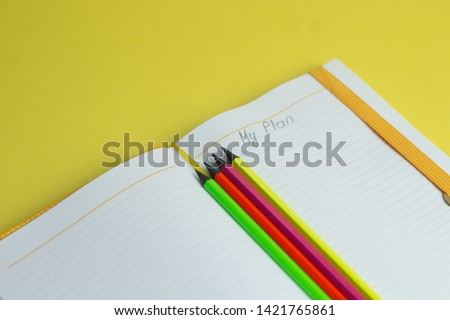 Notebook with my plan text and colored pencils on yellow background, top view, flat lay.