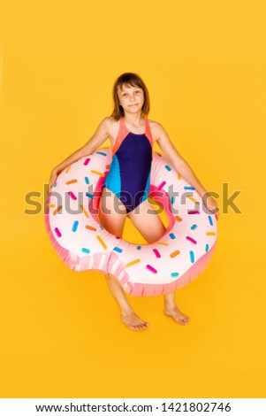 Cute girl in blue swimsuit with huge nflated rubber ring on yellow colour background.