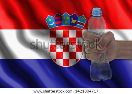 Concept of stopping plastic pollution. Ban disposable products. A hand squeezes a plastic bottle to protest the use of disposable plastic containers against the background of the flag of Croatia