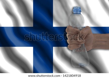 Concept of stopping plastic pollution. Ban disposable products. A hand squeezes a plastic bottle to protest the use of disposable plastic containers against the background of the flag of Finland
