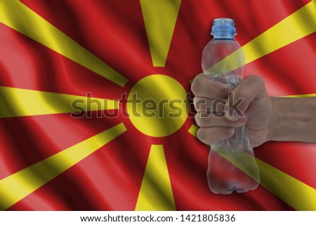 Concept of stopping plastic pollution. Ban disposable products. A hand squeezes a plastic bottle to protest the use of disposable plastic containers against the background of the flag of North Macedon