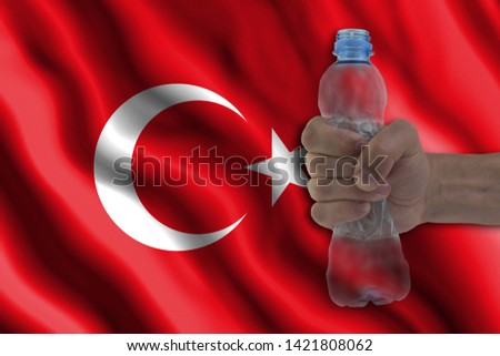 Concept of stopping plastic pollution. Ban disposable products. A hand squeezes a plastic bottle to protest the use of disposable plastic containers against the background of the flag of Turkey