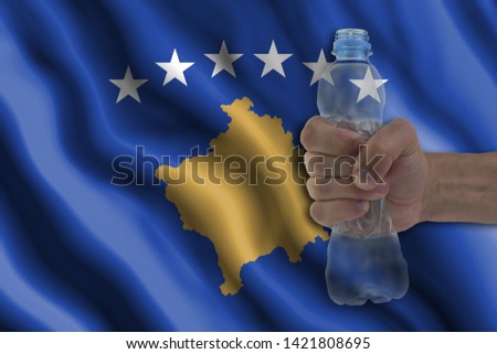 Concept of stopping plastic pollution. Ban disposable products. A hand squeezes a plastic bottle to protest the use of disposable plastic containers against the background of the flag of Kosovo