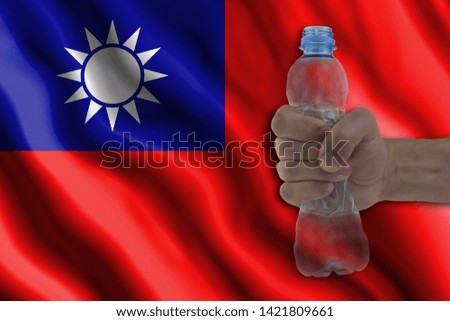 Concept of stopping plastic pollution. Ban disposable products. A hand squeezes a plastic bottle to protest the use of disposable plastic containers against the background of the flag of Taiwan