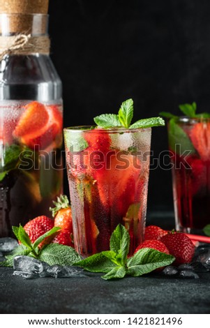 Fresh lemonade with ice, mint and strawberry on top in glass on black table background. Cold summer drink. Sparkling glasses with berry cocktail