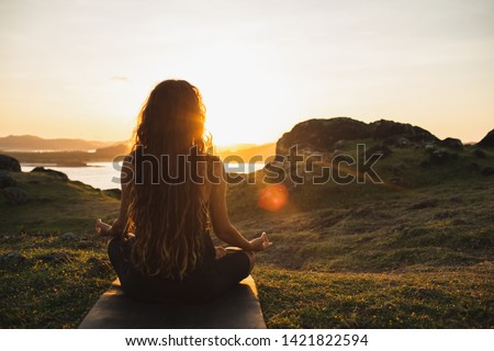 Woman meditating yoga alone at sunrise mountains. View from behind. Travel Lifestyle spiritual relaxation concept. Harmony with nature. Royalty-Free Stock Photo #1421822594