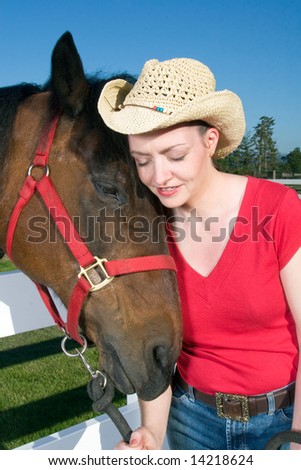 Smiling woman wearing a cowboy hat nuzzles next to a brown horse. Vertically framed photograph.