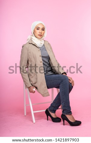 Studio portrait of a fashionable young woman in jeans, long sleeves bush jacket and hijab isolated on pink background. Stylish Muslim female hijab fashion lifestyle portraiture concept.