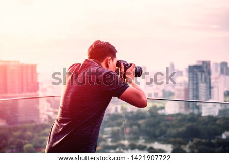 professional photographer man take a photo by DSLR camera,   hipster style man creative photo taking picture sunset city on a rooftop in capital city Thailand, photography by digital device, Asian.