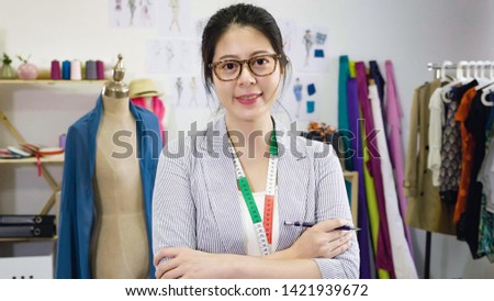 Successful fashion designer asian woman. attractive young japanese lady keeping arms crossed and looking at camera with smile while standing in workshop. beautiful female owner in small business.