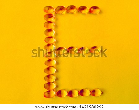 Vitamin E capsule pills in alphabet shape on yellow background. Medicine soft gel tablets of vitamin e tocopherol. Yellow vitamin E cod fish oil medicine supplement capsule - healthy pharmacy concept Royalty-Free Stock Photo #1421980262