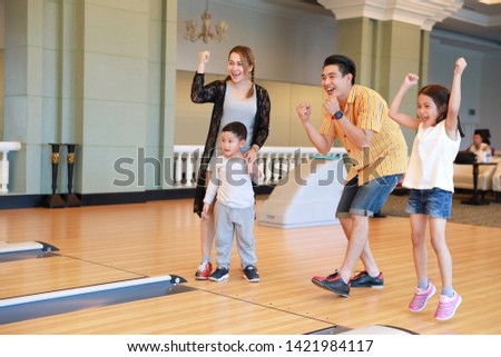 group of happiness asian family father, mother, son and daughter playing bowling in sport club with happy smiling face during holiday vacation