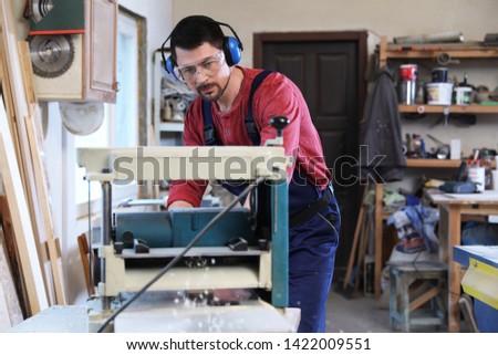 Mature working man using thickness planer at carpentry shop
