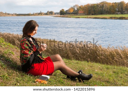 girl on the river bank in the autumn drinks tea reading a book
