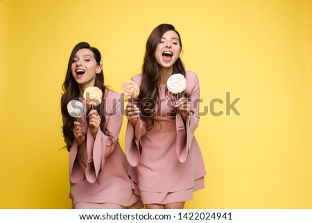 Charming twins closing eyes with lollipops and posing