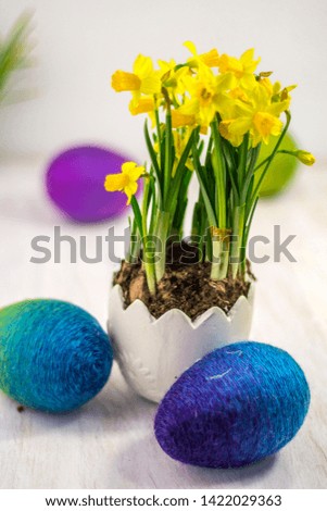Handmade colorful Easter decorations, colorful rainbow Easter eggs with daffodils in a pot imitating eggshell on bright background.
