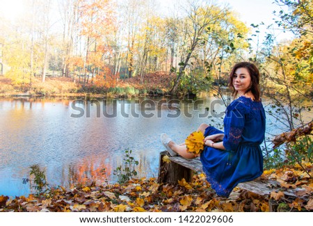 girl in a blue dress on a background of bright autumn maple near the river on a bench