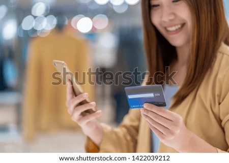 Closeup Asian woman using credit card with mobile for online shopping in department store over the clothes shop store background, technology money wallet and online payment concept, credit card mockup