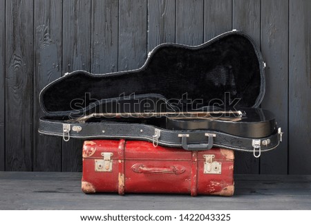 black guitar and a suitcase against a black wooden background
