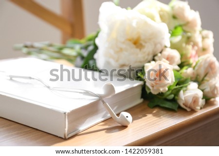 Book, modern earphones and flowers on chair, closeup. Concept of audiobook