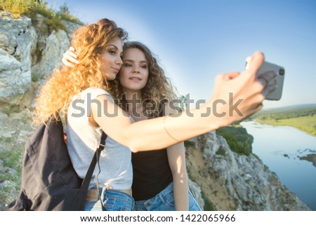 A world without borders. Stunning journey of two girls in the mountains. two attractive young girls travel together, do selfie on the phone against the sky and landscape in the mountains in the sun