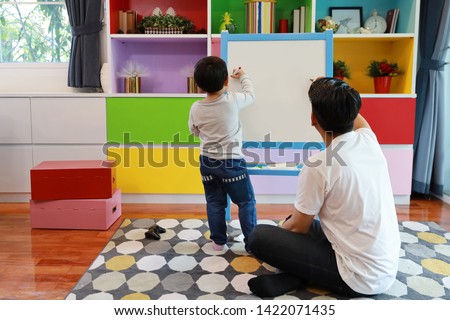Happy Asian family single dad teaching his son how to drawing picture on white board in the living room with happy smiling face (eduction concept)