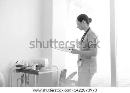 Black and White photo of Mid adult nurse checking medical reports on clipboard at hospital