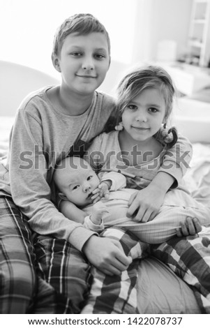 big brother and sister playing with baby brother at home